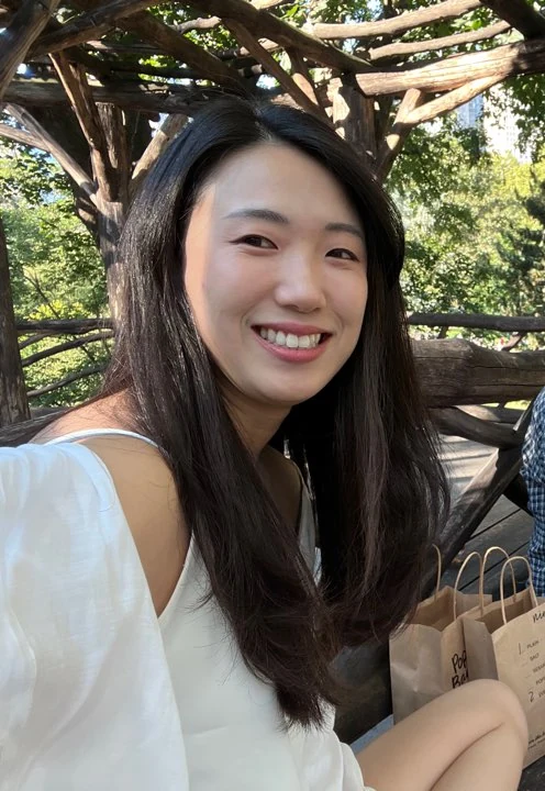Wonder canthoplasty and under-eye fat repositioning: three-month photo diary · Case 058 at Answer Plastic Surgery. Smiling outdoor portrait — 3 months, wonder canthoplasty and under-eye fat repositioning at Answer Plastic Surgery (case 058).